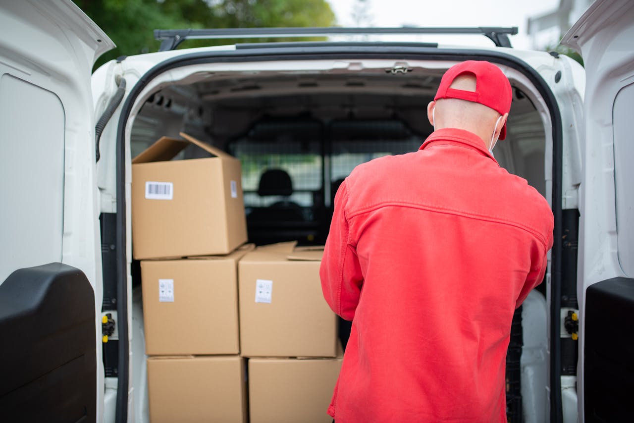 Courier in red loading cardboard boxes into a delivery van outdoors in Portugal.